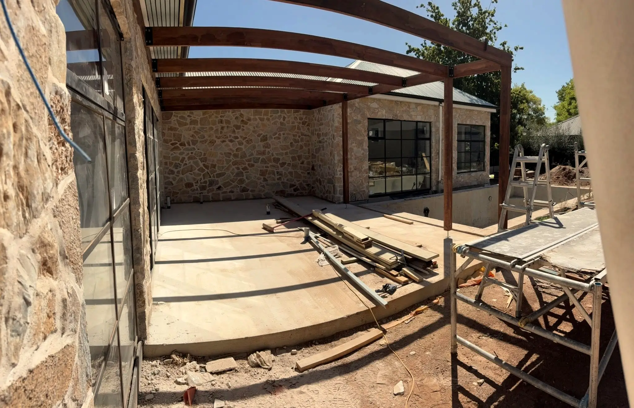 A stone-walled carport under a timber pergola, mid-build.
