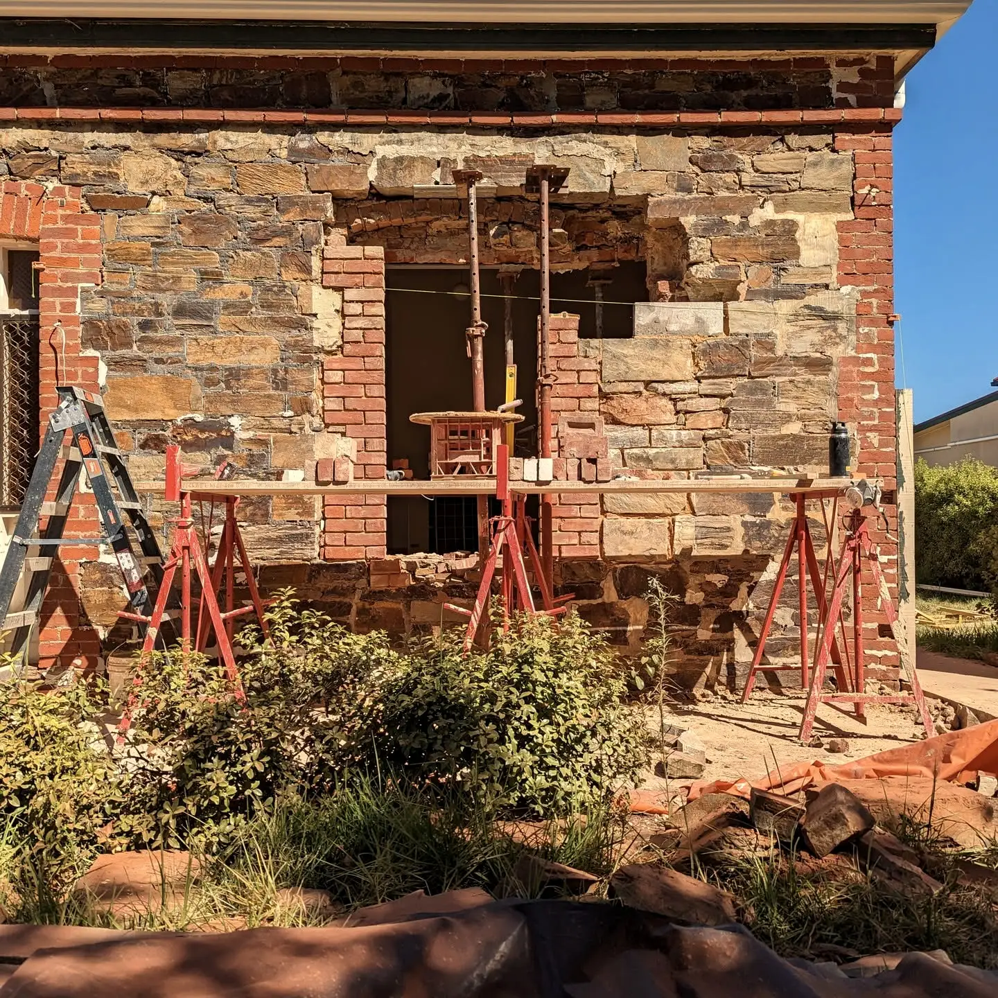 A newly formed window opening in a stone wall, propped on acrow supports with fresh red brickwork around it.