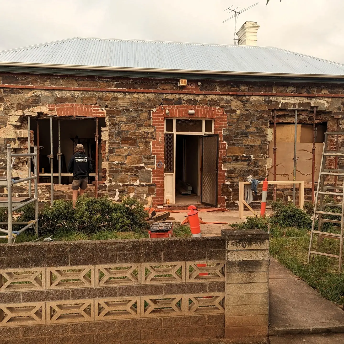 The cottage mid-restoration, paint stripped from the stonework and scaffolding across the front elevation.