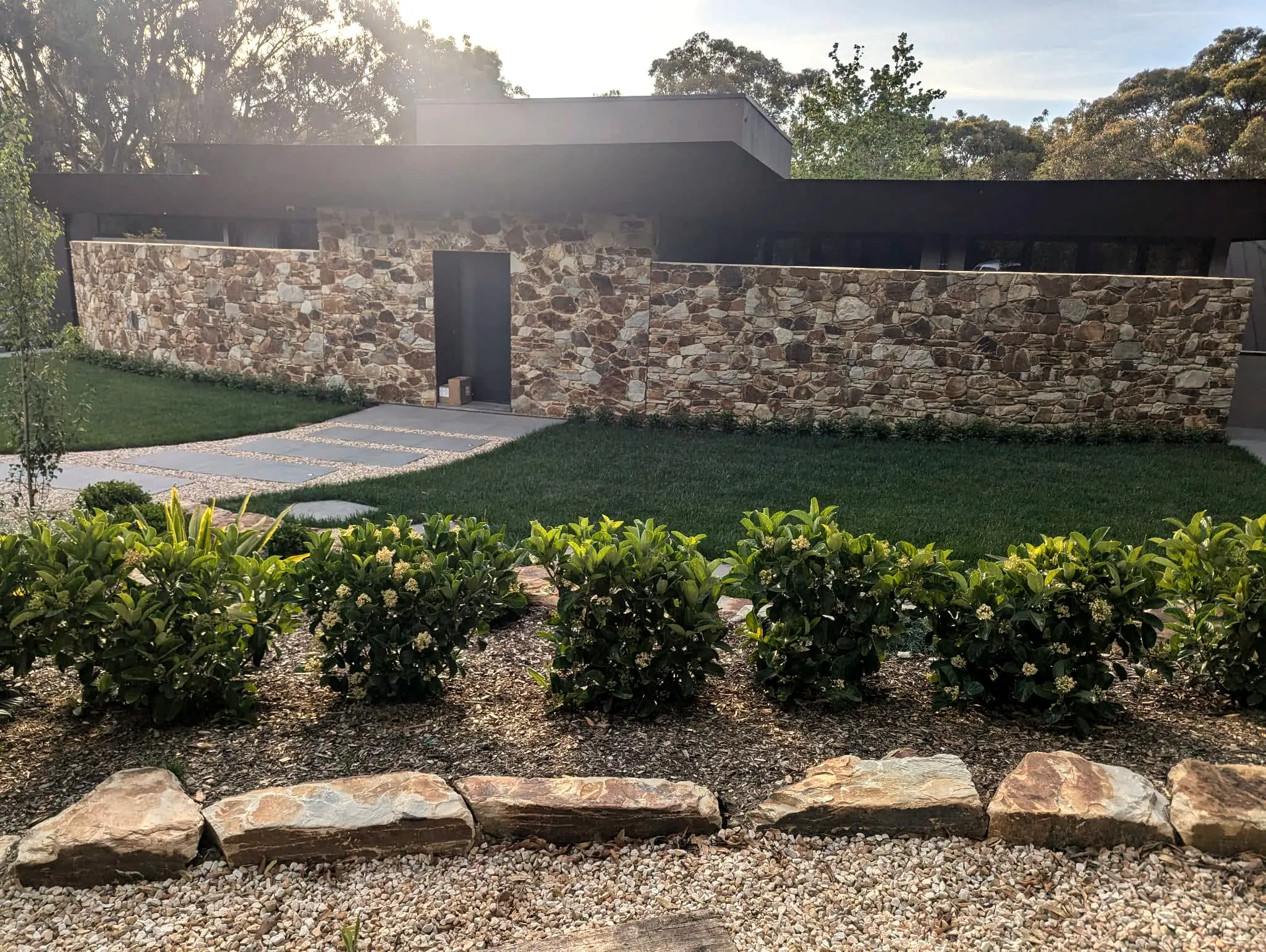 A long dry-laid sandstone wall running the length of a garden, with clipped hedging and lawn in front of a low modern house.