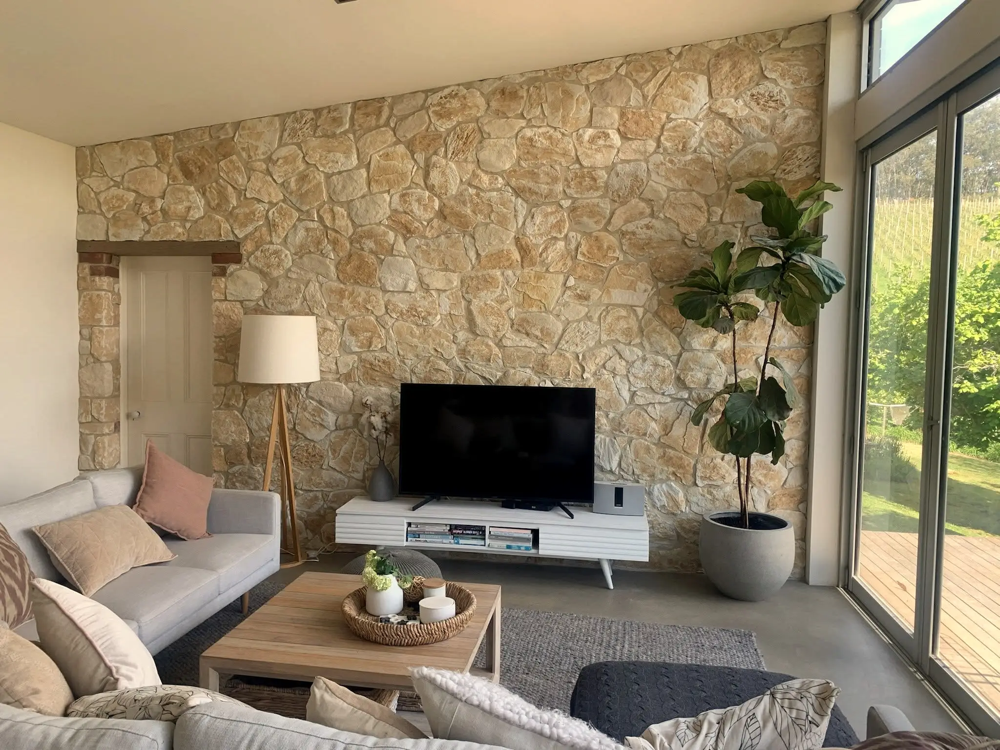 A sandstone feature wall running the full height of a living room, with the garden beyond the glass doors.