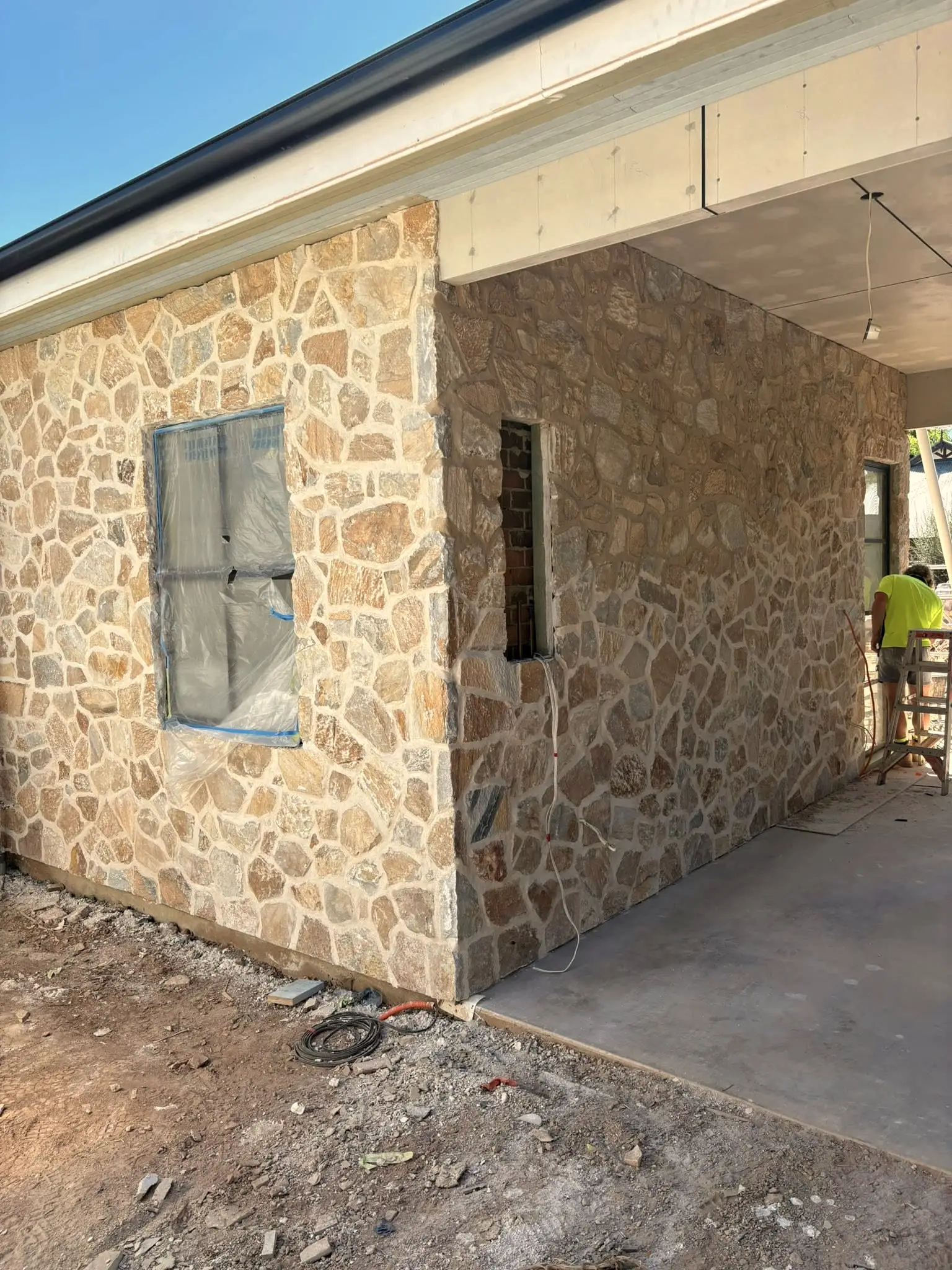 The corner of a new stone building under construction, stonework carried around the return.